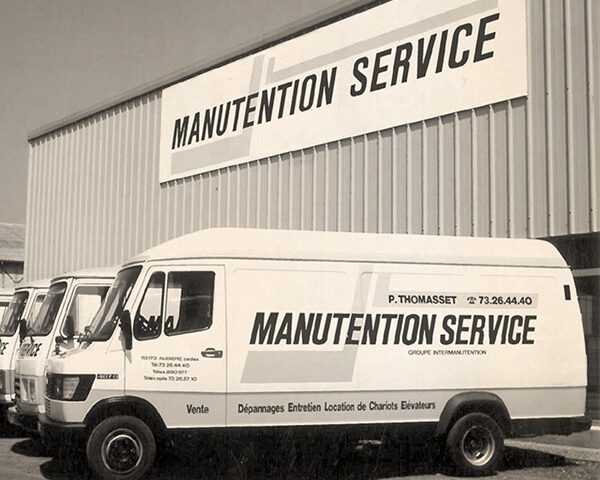 Image en noir et blanc montrant les camions floqués Manutention Service et leur bâtiment derrière